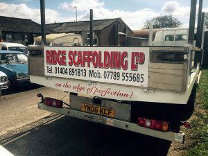 An image of the backside of a white truck. On the door is the Ridge Scaffolding logo and the telephone and mobile numbers for the business.